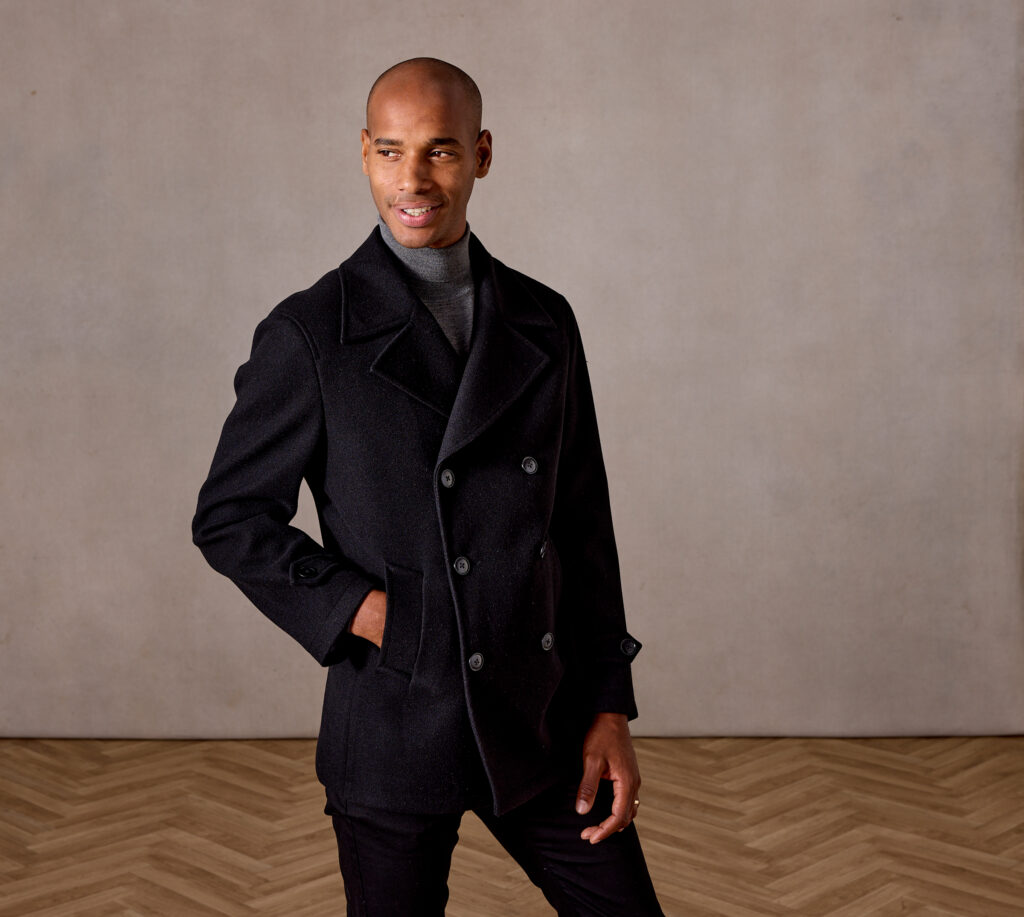 The man is wearing grey turtleneck sweather and black, double breasted jacket